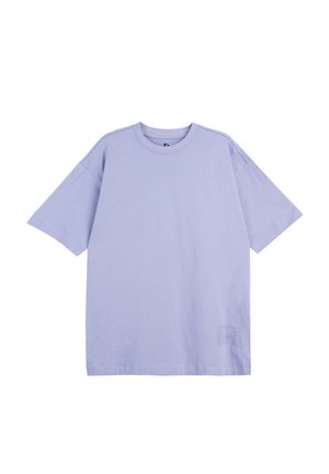 Jasnofioletowa, oversize koszulka z krótkim rękawem, okrągłym dekoltem i subtelnym wypukłym napisem w pobliżu dolnego brzegu na białym tle.