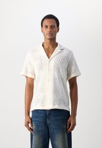 Korte mouwen, open kleurige shirt van gestructureerde, gebreide stof in off-white met een golfpatroon, gecombineerd met blauwe denim jeans.