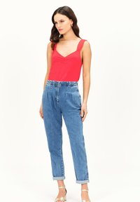 Rode mouwloze top met een V-hals en gathers, gecombineerd met hoogstaande lichtblauwe denim jeans met opgerolde mouwen en strap sandalen.