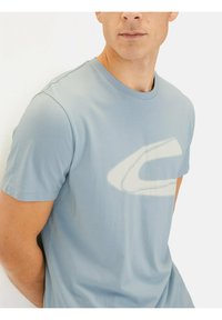 Lyseblå kortærmet t-shirt lavet af bomuld, med et stort hvidt grafisk logo på fronten, rund halsudskæring og blød tekstur.