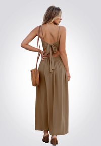 Abito lungo color verde oliva con dettagli di legatura sul retro, spalline sottili e una silhouette fluida. Abbinato a una borsa rotonda intrecciata e sandali con tacco marroni.