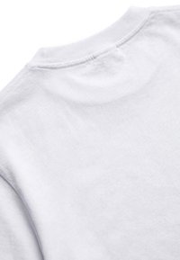 Gros plan de l'encolure arrière d'un t-shirt blanc uni à col rond montrant la texture du tissu et les détails des coutures.