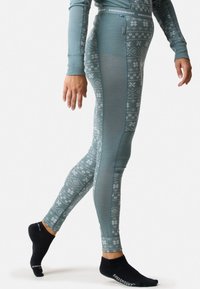 Thermo leggings in een gedempte teal kleur met witte sneeuwvlokpatronen. Beschikt over een aansluitend ontwerp en een elastische tailleband voor comfort.