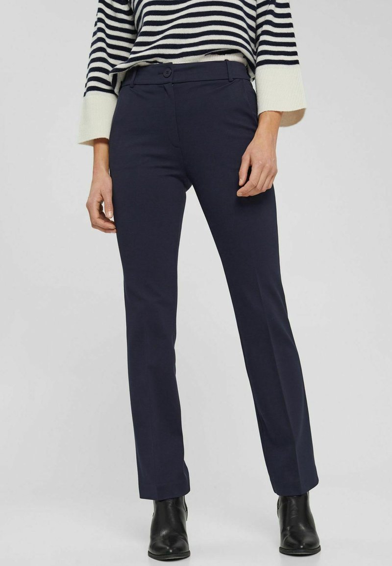 Personne portant un pantalon droit bleu marine, des bottines noires et un pull à manches longues rayé noir et blanc.