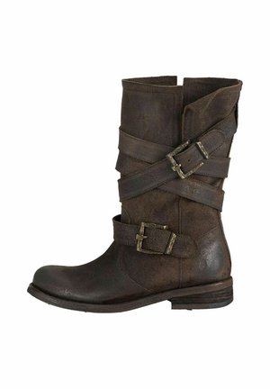 Brązowy skórzany botek do kostki z płaskim obcasem. Posiada wiele zapinanych pasków i postarzany wygląd. Okrągły nosek i lekko zgarbiony fason.