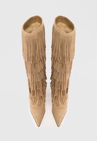Bottes en suède beige hauteur genou avec des franges superposées et un bout pointu. Doublure intérieure lisse.