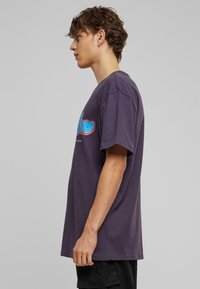 T-shirt en coton violet avec un grand imprimé graphique coloré sur le devant. Manches courtes, coupe droite et silhouette décontractée.