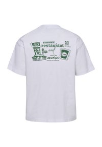 Hvit t-skjorte med grønt trykk av et stadion, restaurantskilt, sportsbar lounge-tekst og små grafiske elementer på baksiden.