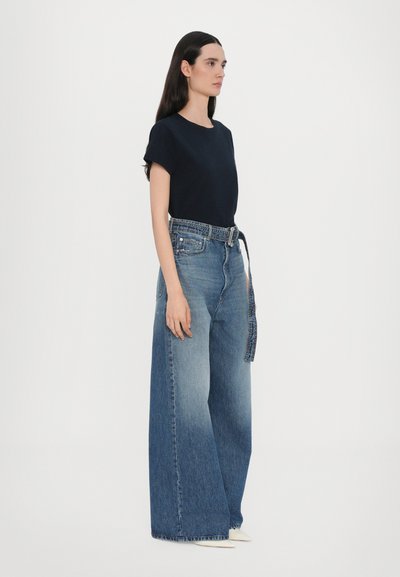 Marineblauw T-shirt met korte mouwen, gecombineerd met wijde medium wash denim jeans met een contrasterende riem en een gespeelde zoom. Soepele textuur, relaxte pasvorm.