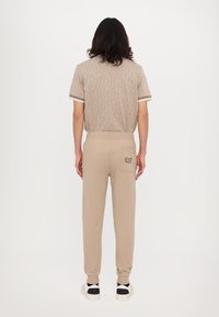 Beige kortermet skjorte med teksturert mønster og kontrastkant, kombinert med elastiske bukser med baklomme og logo.