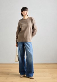 Brun genser med rund hals og avslappet passform, kombinert med vide blå jeans. Tilbehør inkluderer en liten beige håndveske.