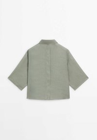 Chemise verte à manches courtes avec une coupe droite, col, couture au dos et tissu texturé, conçue pour un port décontracté.