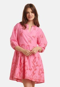 Kurzes pinkes Kleid mit V-Ausschnitt, dreiviertellangen Ärmeln und floralem roten Stickmuster. Fließender, geraffter Taillenbereich, weicher Stoff.