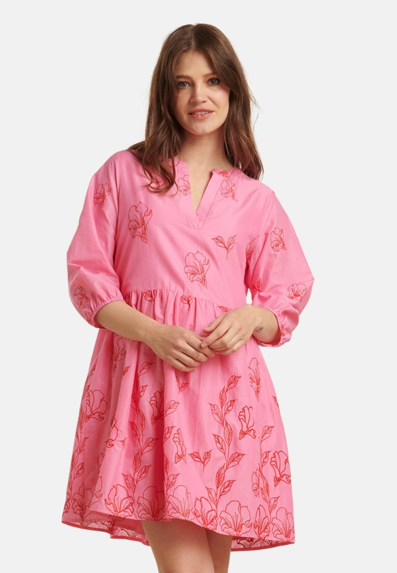 Kurzes pinkes Kleid mit V-Ausschnitt, dreiviertellangen Ärmeln und floralem roten Stickmuster. Fließender, geraffter Taillenbereich, weicher Stoff.
