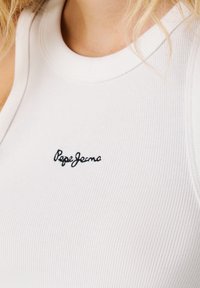 Witte geribbelde tanktop met een ronde halslijn en een zwart geborduurd "Pepe Jeans" logo op de linkerborst. Zachte textuur.