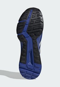 Semelle de chaussure en caoutchouc noir robuste avec un motif de traction bleu. Présente des rainures et des zones surélevées pour une meilleure adhérence et durabilité.