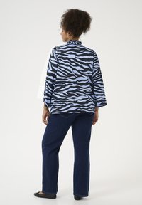 Modrá a černá zebra pruhovaná blůza s vysokým límcem a širokými rukávy, v kombinaci s tmavě modrými rovnými džíny a černými balerínami.