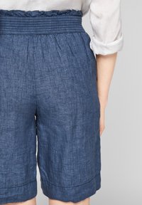 Pantalones cortos de lino en azul oscuro con cintura fruncida y dobladillo en punta. Presentan un acabado texturizado y un corte relajado.