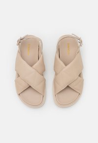 Beige sandaalit, joissa on päällysteinen muotoilu, ristiin menevät hihnat ja nilkkahihna, jossa on hopeinen solki. Sujuva, synteettinen materiaali.