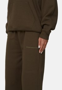 Sweatshirt marron avec une poche à l'avant et un pantalon marron ample arborant le texte "GOODFORNOTHING" sur la cuisse. Tissu au toucher doux.