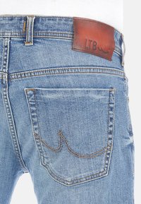 Jeans de mezclilla en azul claro que presentan una etiqueta de cuero marrón de LTB en la cintura, con costuras detalladas y un diseño de bolsillos distintivo.