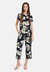 Marineblauer Blumenschnitt-Overall mit kurzen Ärmeln, der über eine lockere Passform, einen elastischen Bund und Taschen verfügt. Betont durch große grüne und weiße Blumen.