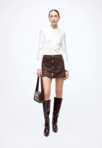 White button-up shirt, brown suede mini skirt with gold buttons, black knee-high glossy boots, and a matching handbag. Simple, elegant design.