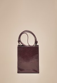 Torbica od kože boje bordo s sjajnim završetkom. Pravokutnog oblika, s dva gornja ručka i utisnutim logotipom marke sprijeda. Jednostavan dizajn.