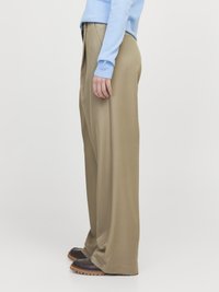 Hosen mit weitem Bein aus leichtem, khakifarbenem Stoff, mit glatter Textur und hoher Taille, kombiniert mit dunkelbraunen Schuhen.
