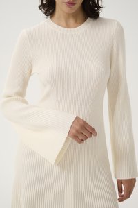 Krämfärgad ribbad klänning med rund hals, långa klockärmar och figurnära midja. Det strukturerade tyget ökar den visuella intresset.