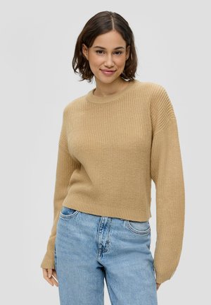 Beige gebreide trui met een ribbelstructuur, ronde halslijn en lange mouwen, gecombineerd met lichtblauwe jeans.