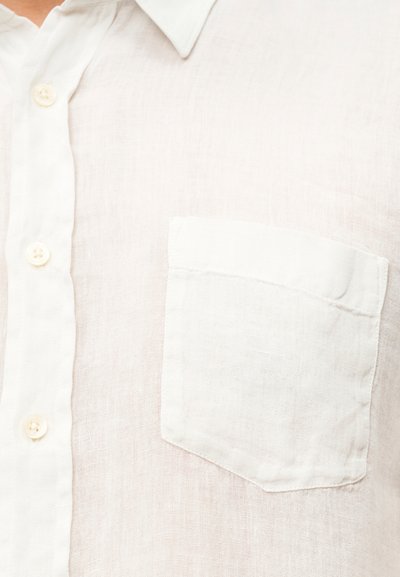 Ανοιχτό μπεζ λινό πουκάμισο με μυτερό γιακά, μια μονή τσέπη στο στήθος και μπεζ κουμπιά. Το ύφασμα έχει υφή και διαπνέουσα εμφάνιση.