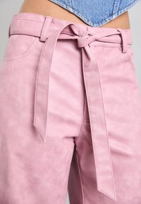 Rosa fusk läderbyxor med en knuten midjebälte, med en mjuk textur och sidofickor, stylade med en hög midja.