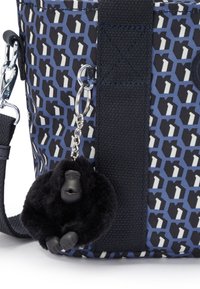 Borsa con motivo blu e una spessa tracolla nera, con un portachiavi a forma di gorilla in peluche nero attaccato a un anello d'argento sul lato.
