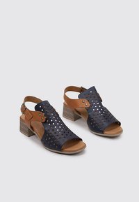 Sandales en cuir avec une tige navy présentant un design perforé, des accents marron et un talon bloc. Style ouvert avec une sangle arrière réglable.