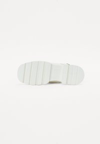 Scarpa bianca con suola in gomma testurizzata e motivo ondulato, punta arrotondata e un semplice design con fibbia per una vestibilità regolabile.