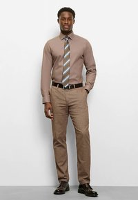 Light brown dress shirt with a collared neckline, paired with tan trousers; features a striped tie in blue and brown, and black shoes.