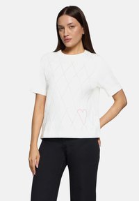 Hvid kortærmet top med diamantm�ønster og pink hjerteaccent. Lavet af glat stof, med en afslappet pasform og rund halsudskæring.