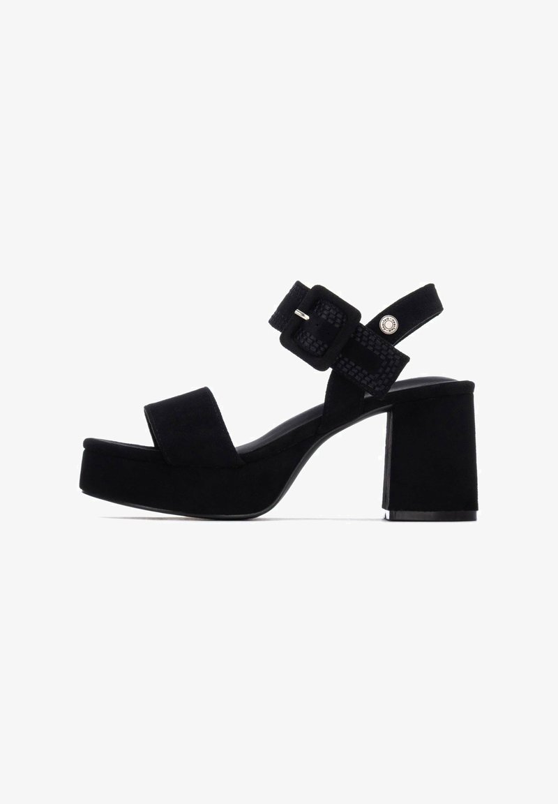 Sandalias de plataforma de gamuza negra con tacón grueso, banda frontal ancha y pulsera ajustable en el tobillo con detalles texturizados.