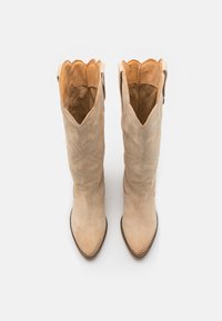 Beige Wildleder-Cowboy-Stiefel mit spitzer Zehenform, gewelltem Kragen und geprägt dekorativem Muster. Verziert mit Nähdetails.