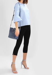 Top azul claro con mangas acampanadas, combinado con pantalones negros cortos. Los accesorios incluyen un bolso azul y sandalias de tacón azul claro.