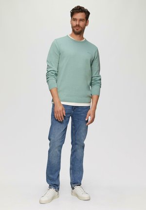 Mintgroene trui met een ronde halslijn en ribgebreide manchetten, gecombineerd met blauwe spijkerbroeken en witte sneakers. Eenvoudig en casual ontwerp.