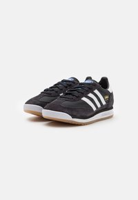 Svarta mocka- och syntetiska sneakers med vita ränder, rund tå, beige sula och blå detaljer på tungan, med en texturerad yta.