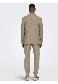 Traje de lino color beige claro con un corte ajustado. La chaqueta tiene una abertura simple y los pantalones tienen un corte recto. Completado con zapatillas blancas.