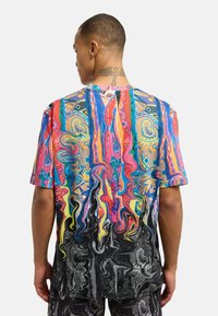 Fargerik t-skjorte med korte ermer og et sirkulært abstrakt mønster, som har sterke toner av rosa, blått og svart. Laget av et lett stoff.