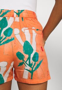 Oranga bomullsshorts med ett grafiskt botaniktryck i grönt och vitt. Inkluderar sidfickor och resårmidja.