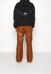 Veste à capuche noire avec détails et logo blancs, associée à un pantalon large en simili cuir marron. Caractérisée par une coupe décontractée et une texture lisse.