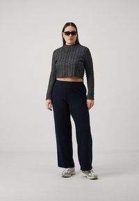 Black and silver ribbed crop top with high neck paired with navy wide-leg pants and gray sneakers. Model stands against a gray background.
