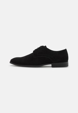 Scarpa da uomo in suede nero con punta arrotondata, design con lacci e suola piatta in gomma, caratterizzata da delicate cuciture sulla parte superiore.