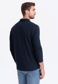 Mörkblå långärmad polo med krage och rak nederkant. Mjuk väv med en slät struktur, figursydd design och minimalistisk stil.